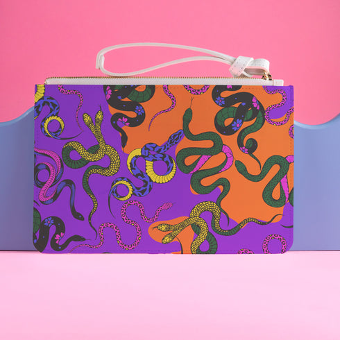 Rectangular wristlet clutch featuring vibrant purple and orange background with colorful snake prints. White strap and gold zipper visible.
