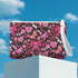 Rectangular wristlet clutch featuring a dark background with pink skull bows, cherries, and other goth-inspired motifs. White strap and gold zipper visible.