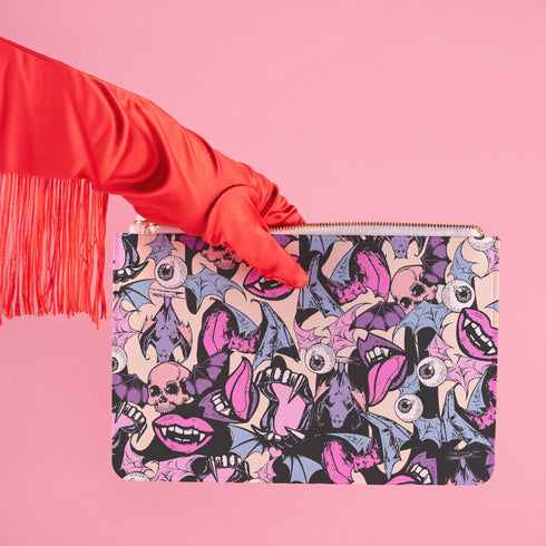 Rectangular wristlet clutch featuring a dark background with colorful bats, skulls, eyeballs, and vampire mouths. White strap and gold zipper visible.