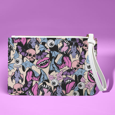 Rectangular wristlet clutch featuring a dark background with colorful bats, skulls, eyeballs, and vampire mouths. White strap and gold zipper visible.