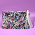 Rectangular wristlet clutch featuring a dark background with colorful bats, skulls, eyeballs, and vampire mouths. White strap and gold zipper visible.