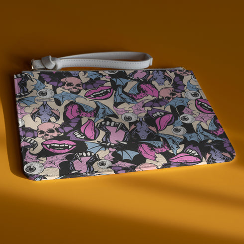 Rectangular wristlet clutch featuring a dark background with colorful bats, skulls, eyeballs, and vampire mouths. White strap and gold zipper visible.