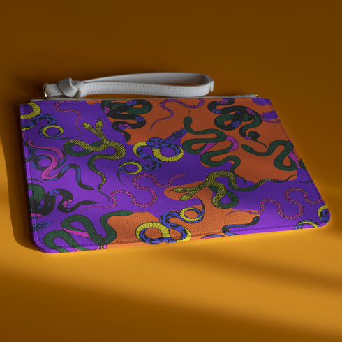 Rectangular wristlet clutch featuring vibrant purple and orange background with colorful snake prints. White strap and gold zipper visible.