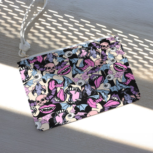 Rectangular wristlet clutch featuring a dark background with colorful bats, skulls, eyeballs, and vampire mouths. White strap and gold zipper visible.