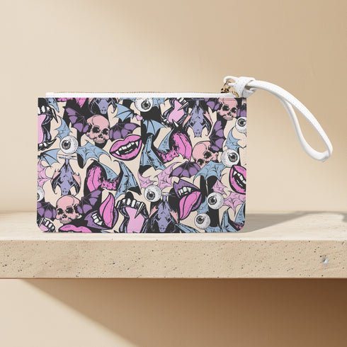 Rectangular wristlet clutch featuring a dark background with colorful bats, skulls, eyeballs, and vampire mouths. White strap and gold zipper visible.