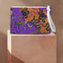 Rectangular wristlet clutch featuring vibrant purple and orange background with colorful snake prints. White strap and gold zipper visible.