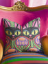 A square decorative pillow cover featuring a vibrant, symmetrical flat printed design that mimics the look of textured embroidery. Two black cats with large yellow eyes and pink noses face forward against a bright red background. Below the cats are large purple and pink flowers with green stems. Above the cats are green cactus shapes. The artwork uses bold, colorful outlines to create an optical illusion of stitching, though the fabric itself is smooth.