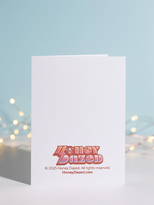 A vertical 5x7 holiday card featuring a retro tattoo style illustration of Krampus in pastel pink, teal, and black ink on shimmery silver pearlescent paper. The central horned demon has a long tongue and is surrounded by vintage rotary phones, daggers, candy canes, and skull gifts. Top text asks Have You Been Good while the bottom banner reads Krampus Is Calling. The interior text reads Let's be honest... Being good is overrated. Merry Christmas.