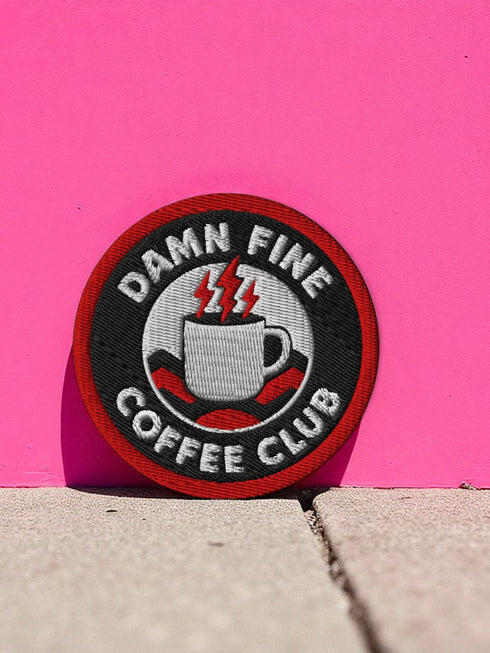 A round, 3-inch embroidered patch with a thick, red merrowed border for a clean, finished edge. The design features a solid black background with the words 'DAMN FINE' in an arc at the top and 'COFFEE CLUB' in an arc at the bottom, all in a bold, white, sans-serif font. In the center, a detailed white coffee mug with a black handle is depicted. Two bright red lightning bolts emerge from the top of the mug, symbolizing energy, reminiscent of the Black Lodge floor from Twin Peaks.