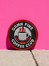 A round, 3-inch embroidered patch with a thick, red merrowed border for a clean, finished edge. The design features a solid black background with the words 'DAMN FINE' in an arc at the top and 'COFFEE CLUB' in an arc at the bottom, all in a bold, white, sans-serif font. In the center, a detailed white coffee mug with a black handle is depicted. Two bright red lightning bolts emerge from the top of the mug, symbolizing energy, reminiscent of the Black Lodge floor from Twin Peaks.