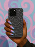 A hand holding a phone case with a spider web design against a colorful background.