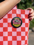 Round pinback button badge with Local Queer Menace text in bold yellow and pink retro lettering on a black background. A cartoon raccoon with a spiked collar flips the middle finger with a painted pink nail, framed by a hot pink sunburst, lightning bolts, and star accents. Glossy laminate finish over durable metal tinplate with a secure safety pin backing. Funny queer pride pin available in 2.25 inch and 3 inch sizes for jackets, totes, lanyards, and backpacks.