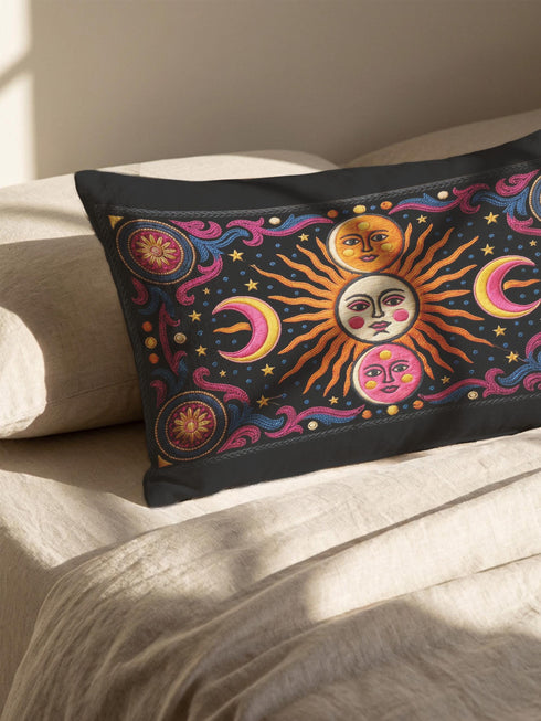 Rectangular 20x12 inch lumbar pillow cover in black featuring printed faux crewel embroidery of a large orange sunburst with a cream face, flanked by pink and yellow crescent moons, a golden moon face above and a pink moon face below, gold stars, blue dots, magenta and blue baroque scroll flourishes, and four corner medallions with golden flowers. Whimsigoth celestial design printed on both sides with a hidden zipper, crafted from soft linen look polyester.