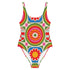 A one-piece swimsuit with a 1970s retro psychedelic geometric pattern in red, orange, green, and blue on a cream background. The swimsuit features a scoop neck and cheeky high-cut fit. In one view, she styles it with a pink baseball cap and gold necklaces. The design includes a central radial sunburst mandala and checkerboard side panels, representing a maximalist, rockstar-ready aesthetic.