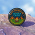 Round glossy pinback button measuring 2.25 inches featuring a playful camp-themed design with the phrase “Camp Counselor for the Gender Crisis.” The artwork includes two orange tents, a rainbow campfire, stars, and green grass. Bottom text reads “Cabin Queer, Unit Psychedelic.” Made from durable tinplate with a safety pin back and coated in a UV and scratch-resistant mylar finish. Bold and colorful, perfect for jackets, bags, or pride outfits.