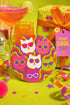 A close-up photograph of a glossy round ceramic coaster featuring a retro 70s psychedelic design. The artwork displays a cluster of six stylized cat face illustrations, each wearing a different pair of sunglasses including retro round and cat-eye shapes. The cats are colored in solid shades of white, hot pink, purple, and lime green. They are set against a vibrant background of wavy, swirling lines in bright orange, red, and purple. The top surface has a highly reflective clear glaze.