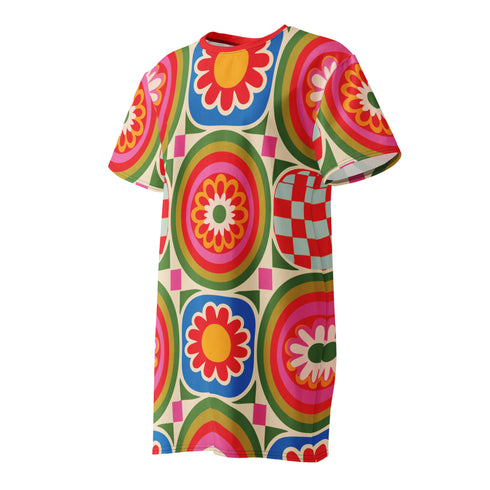 Short sleeve crew neck t-shirt dress on a cream background with an allover retro mod flower medallion print. Bold 60s daisies in red, yellow, and white sit at the center of concentric rainbow rings in lime green, hot pink, orange, and royal blue, with small magenta squares and tiny red checkerboard accents between the motifs. Above-the-knee straight fit silhouette in a 95 percent cotton, 5 percent elastane heavyweight stretch blend. Groovy retro flower power dress for dopamine dressing and easy summer outfi