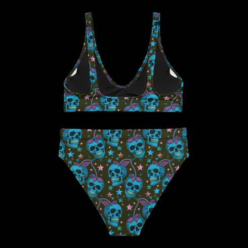 High-waisted bikini set featuring an all-over pattern of neon blue skulls with pink bows, pastel stars, and purple cherries on a dark olive green background. The top has a scoop neckline with wide straps, and the bottoms offer full coverage. A bold, punk-inspired swim look perfect for alternative fashion lovers and dopamine dressers.