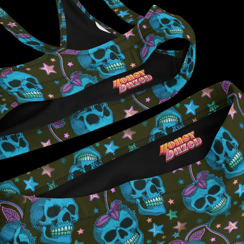 High-waisted bikini set featuring an all-over pattern of neon blue skulls with pink bows, pastel stars, and purple cherries on a dark olive green background. The top has a scoop neckline with wide straps, and the bottoms offer full coverage. A bold, punk-inspired swim look perfect for alternative fashion lovers and dopamine dressers.