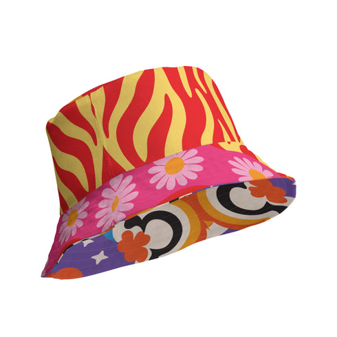 A reversible bucket hat with two distinct sides. Side one features a red and yellow zebra pattern with large pink and orange daisies. Side two has a deep purple background with white stars, rainbow scalloped bands in blue, green, and orange, and retro black and white flowers. The fabric has a visible textured linen weave. The hat is shown in a structured, professional studio shot against a white background, highlighting its 100% polyester durability.