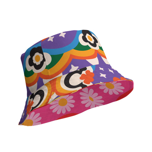 A reversible bucket hat with two distinct sides. Side one features a red and yellow zebra pattern with large pink and orange daisies. Side two has a deep purple background with white stars, rainbow scalloped bands in blue, green, and orange, and retro black and white flowers. The fabric has a visible textured linen weave. The hat is shown in a structured, professional studio shot against a white background, highlighting its 100% polyester durability.