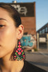 A close-up of a person's face wearing a large, colorful earring with a geometric pattern.