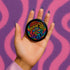 a person's hand holding a small button that says psychedelic made me gay