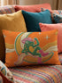 Rectangular 20x12 inch lumbar pillow cover in bright orange featuring printed faux embroidery of a green frog wearing a pink cowgirl hat and pink cowboy boots, lounging on a golden yellow crescent moon shaped like a peeled banana, surrounded by cream and gold sparkle stars and retro wavy stripes. Whimsical cowboy frog design printed on both sides with a hidden zipper, crafted from soft linen look polyester in a funky 70s retro style.