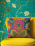 a vibrant yellow chair with a colorful throw pillow featuring a floral design in shades of pink, blue, and yellow. The chair is positioned against a wall with a green and white floral wallpaper.