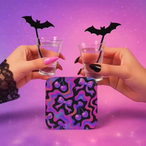 Square drink coaster featuring a bold Y2K-inspired pattern with gradient cherries and shiny pink bows on a black background with psychedelic pink, purple, and blue squiggle lines. Made from hardboard MDF with a non-slip cork backing and a high-gloss topcoat. Measures 3.74 by 3.74 inches. Water-repellent and heat-resistant, ideal for pastel goth, coquette, maximalist, and dopamine decor themes.