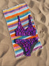 Psychedelic crystal bikini top featuring a vivid print of pink and purple crystals with wavy neon accents on a black background. Sports bra-style top with a scoop neckline, wide shoulder straps, and removable padding. Made of recycled polyester and LYCRA XTRALIFE with UPF 50+ sun protection. Available in sizes XS to 3XL. Double-layered construction with a snug, secure fit. Sustainable swimwear top for rave, beach, or summer festival wear.