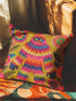 A square faux embroidery pillow featuring a brightly colored maximalist design against a mustard yellow background. In the center stands a stylized, furry Bigfoot or Sasquatch figure rendered in vibrant layers of pink, orange, blue, and lime green with a blue face and yellow eyes. The central creature is surrounded by large, detailed symmetrical pink and blue flowers and leaves. The flat printed fabric creates a highly realistic optical illusion of dimensional crewel embroidery stitches.