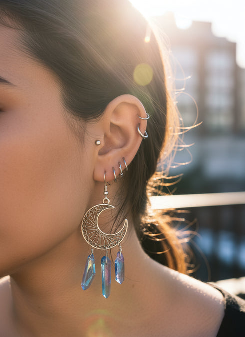 A close-up of a person's ear adorned with multiple piercings and a large, dangling earring featuring blue gemstones.