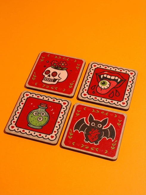 et of four square glazed ceramic coasters featuring a vibrant pastel goth and creepy cute design. These functional art pieces show a spooky yet playful aesthetic perfect for alternative home decor. The coasters have a glossy wipe-clean finish and a non-slip cork backing to protect furniture surfaces from hot and cold beverages. Ideal for maximalist coffee tables, witchy desks, or as a unique housewarming gift for horror fans who love retro 70s and dopamine decor styles.