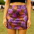 A woman wearing a short skirt with a vibrant floral pattern of purple and orange roses, along with leopard print accents.