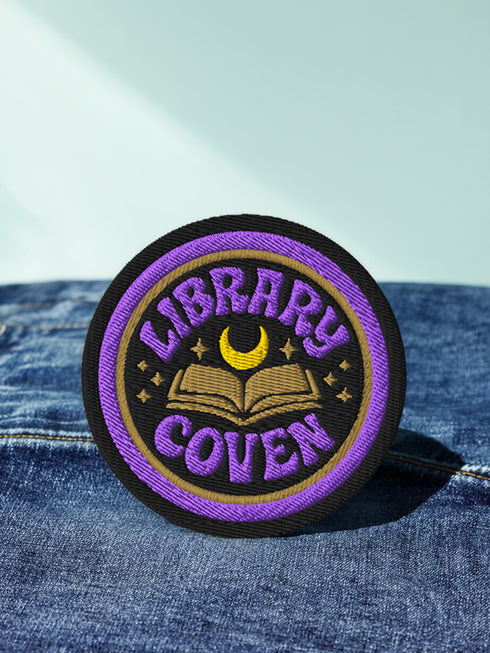 3-inch round embroidered iron-on patch in a cotton–polyester blend; black base with purple ring and gold accent ring; open book, gold crescent moon, tiny stars; curved purple text reads “LIBRARY COVEN”; merrowed edge. Witchy book lover patch for librarians, dark academia, and BookTok covens; makes a great gift for readers, witches, and spooky library pals.