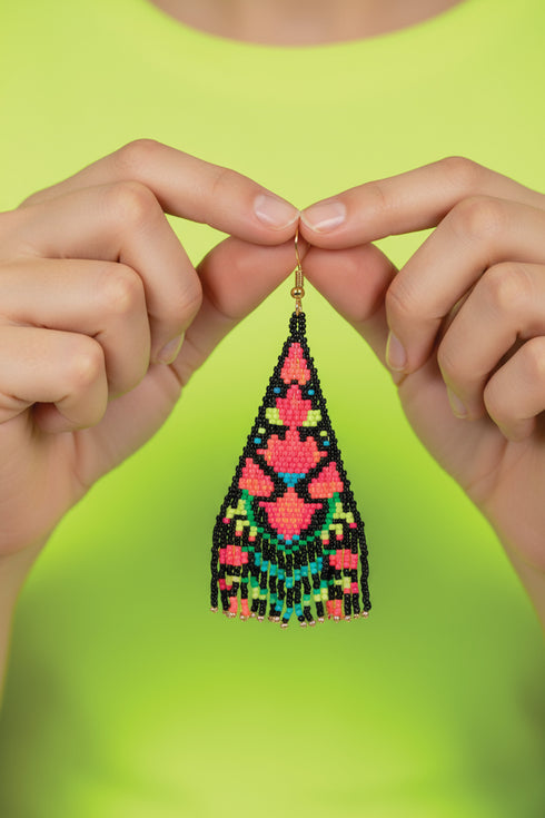 A pair of hands holding a colorful, beaded earring against a bright green background.