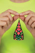A pair of hands holding a colorful, beaded earring against a bright green background.