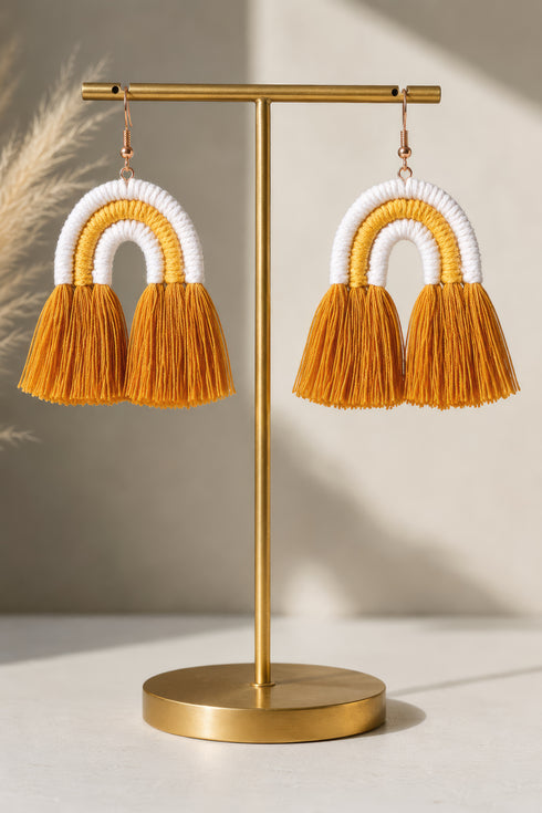 A pair of gold-colored earrings with orange tassels hanging from them, displayed on a gold stand.