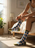 A person is sitting on a bed, adjusting their blue and white patterned socks.