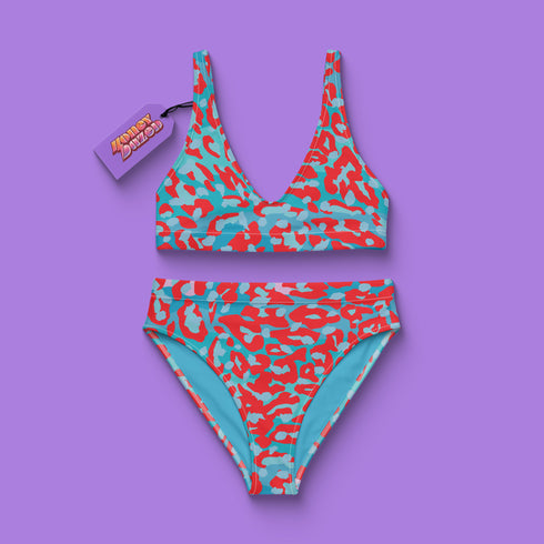 Vibrant two-piece leopard print swimsuit with abstract red and teal pattern. Sports bra-style top and high-waisted bottoms. Purple background. Tag visible. Trendy, colorful beachwear for modern style.