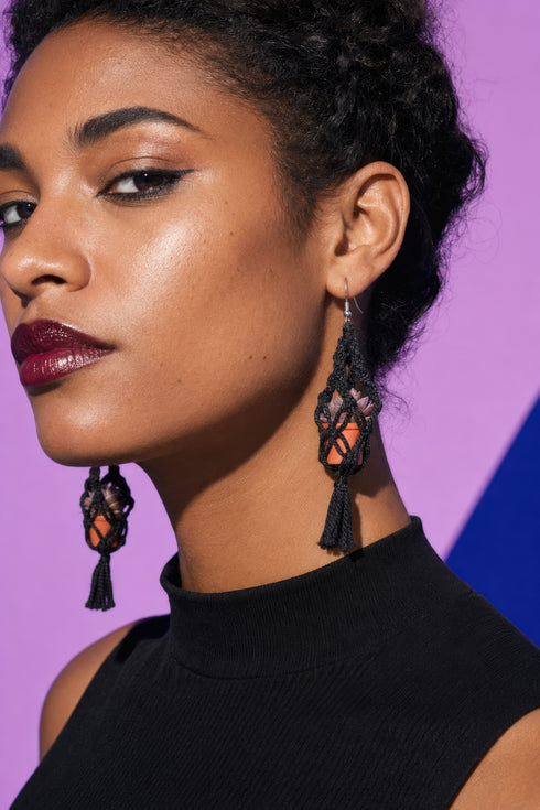 A close-up portrait of a woman wearing large, dangling earrings with a black tassel.