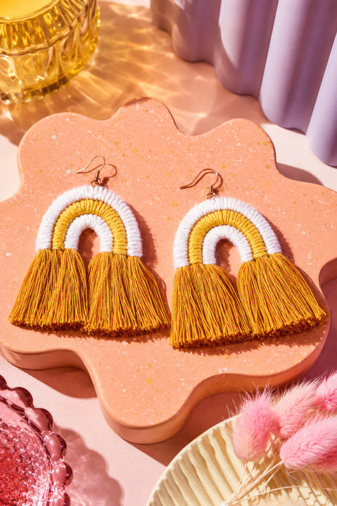 a pair of yellow and white tassel earrings with fringed tassels, displayed on a pink speckled surface.