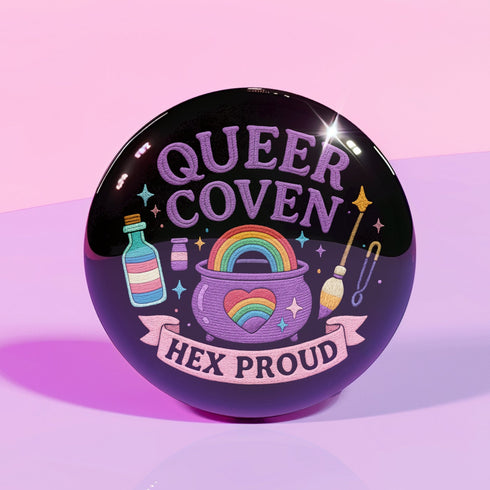 Glossy black pinback button with pastel artwork of a bubbling cauldron, rainbow, potion bottles, and tools. Text reads “Queer Coven, Hex Proud.”