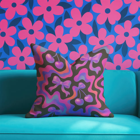 Throw pillow with a black background and a vibrant Y2K-inspired design featuring gradient cherries and shiny bows. The pattern includes pink, purple, orange, and blue psychedelic squiggles. The square pillow is displayed on a pink chair, bright blue couch, and outdoors with camping gear, emphasizing its bold, girly, and playful aesthetic. Perfect for dopamine decor, Gen Z bedrooms, or quirky home styling.