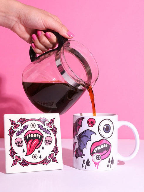 White porcelain 11oz mug and matching 4x4 inch square ceramic coaster set featuring a vibrant, maximalist full-wrap pattern. The design illustrates glossy pink vampire lips with white fangs and red tongues, interspersed with floating eyeballs, purple bats, and small pink skulls against a white background. The mug features a glossy finish and C-handle. The coaster has a matching glazed ceramic top and a brown cork backing. High-contrast pop-art style with pink, purple, and black details.