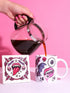 White porcelain 11oz mug and matching 4x4 inch square ceramic coaster set featuring a vibrant, maximalist full-wrap pattern. The design illustrates glossy pink vampire lips with white fangs and red tongues, interspersed with floating eyeballs, purple bats, and small pink skulls against a white background. The mug features a glossy finish and C-handle. The coaster has a matching glazed ceramic top and a brown cork backing. High-contrast pop-art style with pink, purple, and black details.