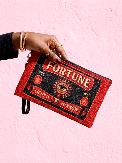 A rectangular red zippered pouch featuring a vintage-style tarot card design. The front displays the word FORTUNE in large beige capital letters. A central illustration shows a mystic eye emitting rays of light above a lit candle flame. The text YES and NO appears on the sides. A banner at the bottom reads LIGHT IT TO KNOW. The bag is crafted from red polyester with a linen-like woven texture, featuring a black zipper and a removable black nylon wrist strap. The interior is white.