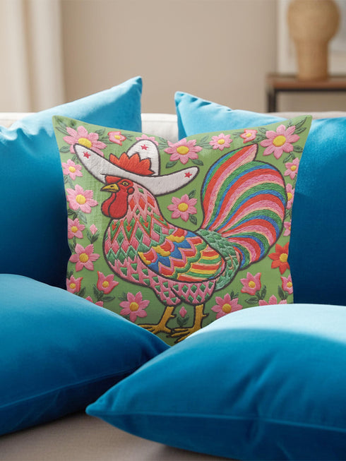 Square throw pillow cover with a printed faux embroidery design of a rooster wearing a white cowboy hat with red stars on a grass green background. The western chicken has a red comb and wattle, yellow beak and feet, and layered feathers in pink, green, orange, blue, and yellow with a rainbow striped tail. Pink and red flowers with yellow centers frame the bird. The stitched look is a flat 2D print on a smooth linen feel polyester cover with a hidden zipper, not raised embroidery.