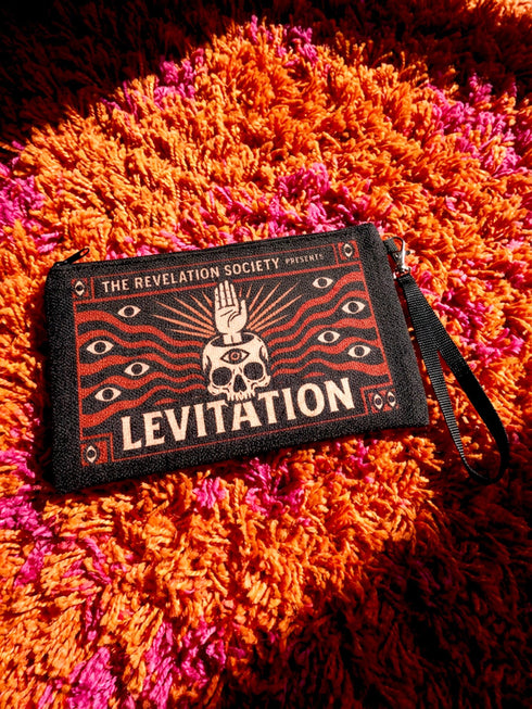 A rectangular makeup bag featuring a vibrant psychedelic print with gothic elements. The fabric texture is clearly visible showing a woven linen-like polyester grain. A black zipper runs across the top edge with a black detachable nylon wrist strap clip on the side, showcasing the approximately nine by six inch dimensions. The print includes high contrast neon colors and trippy swirling patterns typical of maximalist decor.